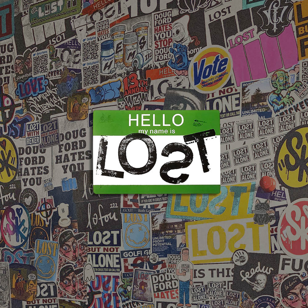 Hello my name is LOST sticker. A green and white nametag sticker stamped with the name LOST with a backwards S. The sticker is set against a colorful wall of graffiti stickers.