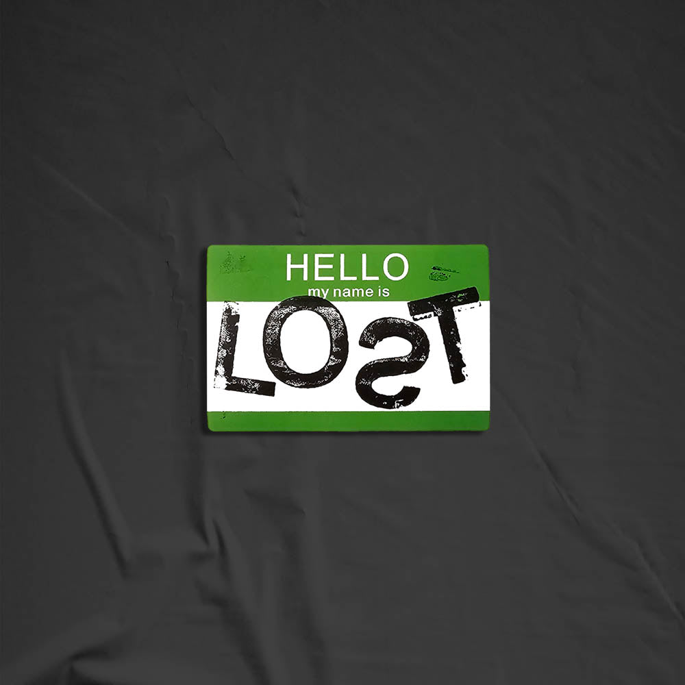 Hello my name is LOST sticker. A green and white nametag sticker stamped with the name LOST with a backwards S. The sticker is set against a black background.