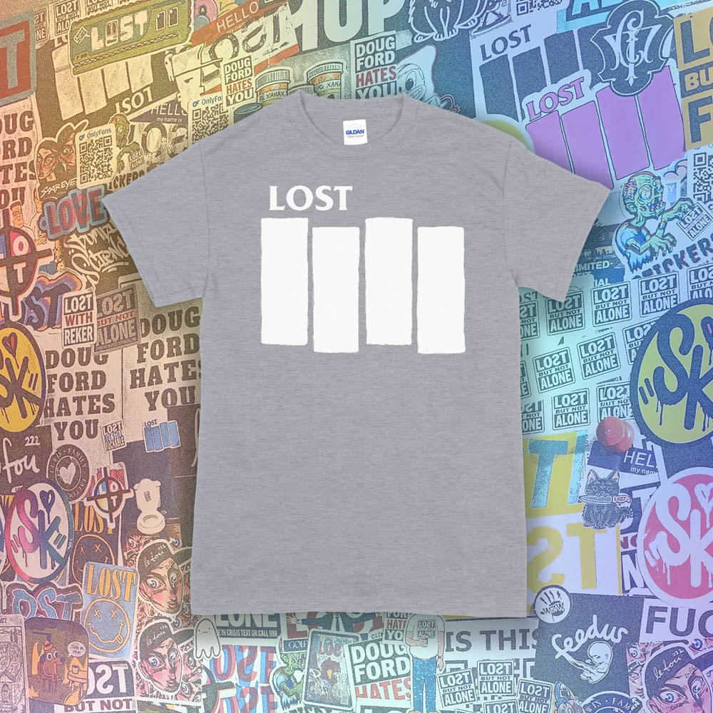 The Lost Flag t-shirt. The iconic bold logo is screen printed in white ink on a light grey cotton shirt. A collection of colorful graffiti stickers from artists around the world decorate the background.