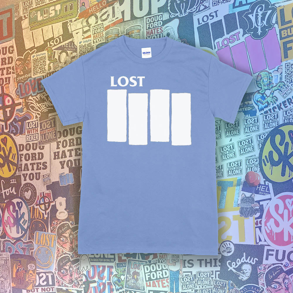 The Lost Flag t-shirt. The iconic bold logo is screen printed in white ink on a light blue cotton shirt. A collection of colorful graffiti stickers from artists around the world decorate the background.