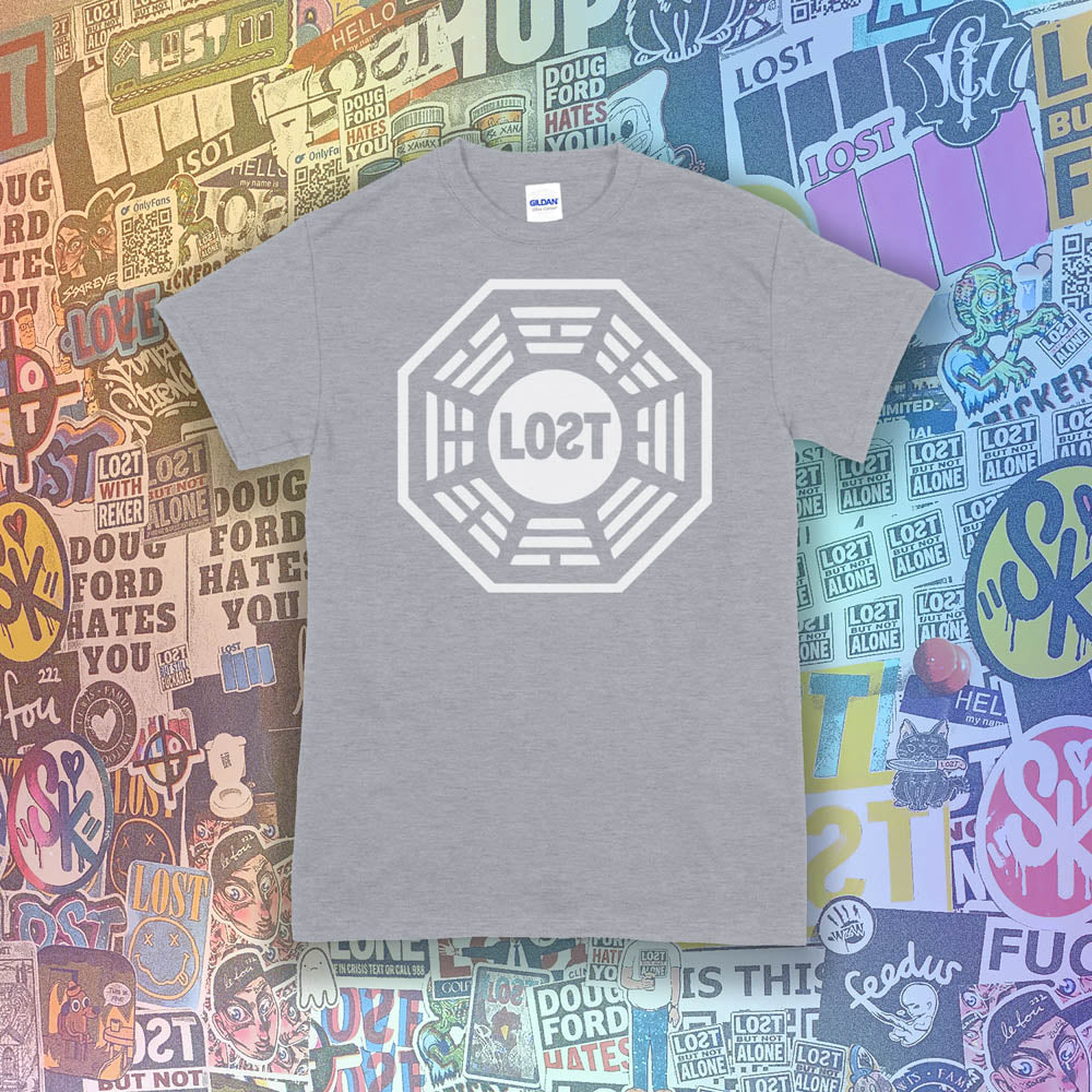 The Lost Initiative t-shirt with a large solid white logo screen printed on a light grey shirt. A collection of colorful graffiti stickers from artists all over the world make up the background.