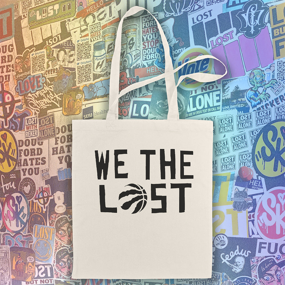 We the LOST printed in bold black lettering with the raptor claw design displayed on a natural canvas tote bag. A wall of colorful graffiti stickers by graffiti artists from around the world creates a vibrant background for the tote bag on display.  
