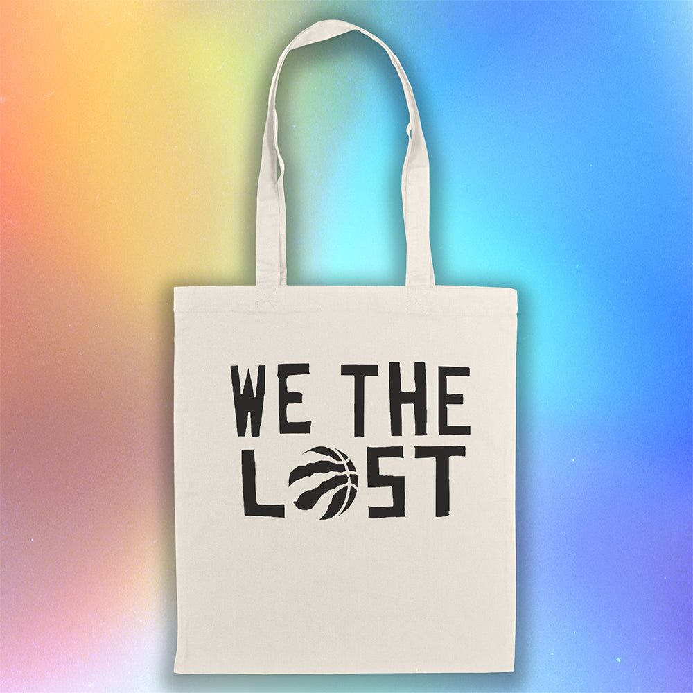We the LOST printed in bold black lettering with the raptor claw design displayed on a natural canvas tote bag. A holographic background creates a neutral atmosphere for the tote bag on display.  