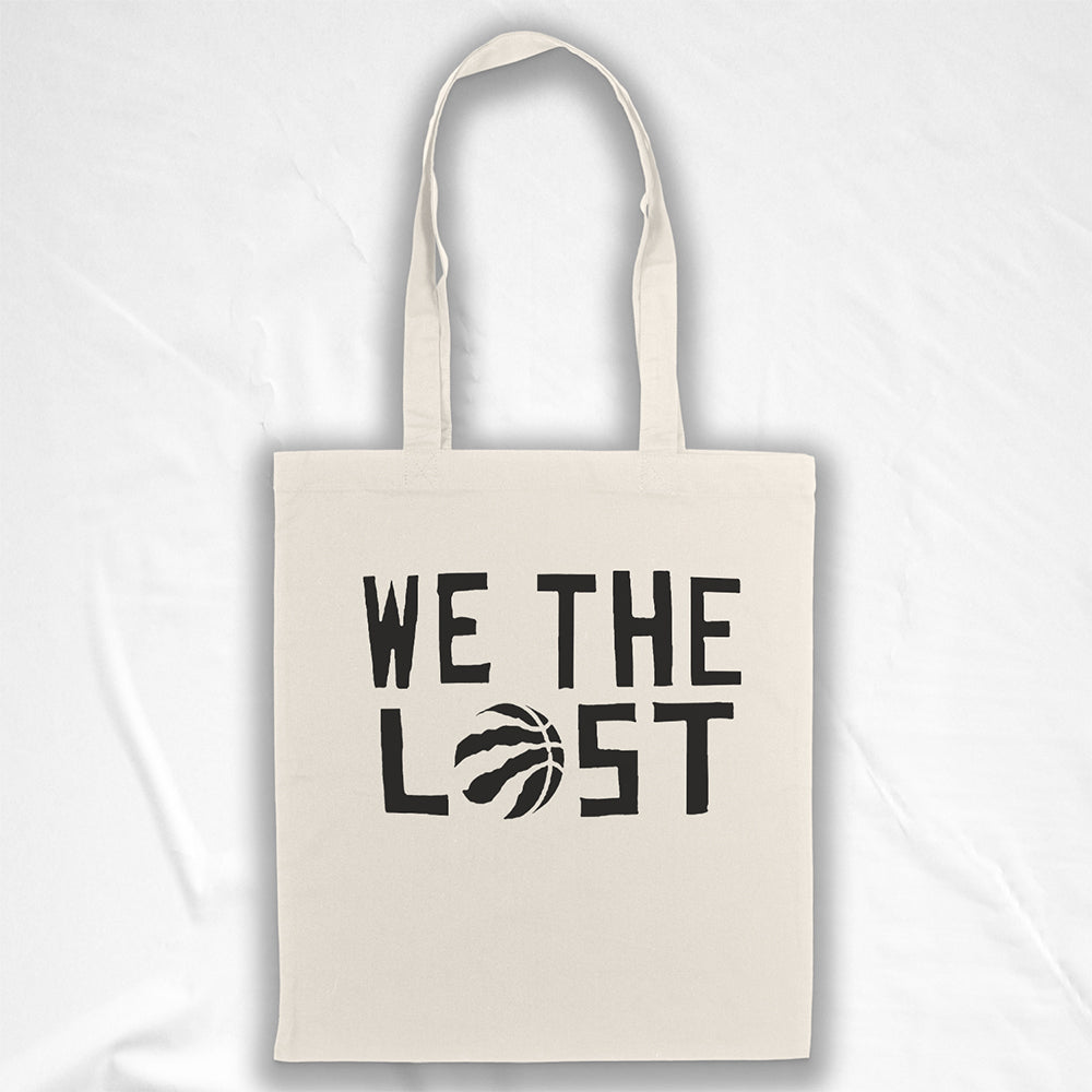 We the LOST printed in bold black lettering with the raptor claw design displayed on a natural canvas tote bag. A plain white background provides a neutral setting for the tote bag on display.  
