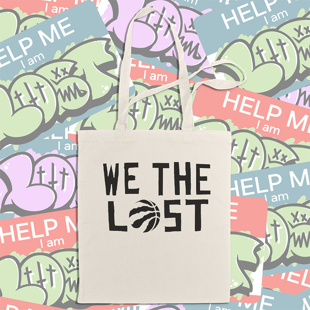 We the LOST printed in bold black lettering with the raptor claw design displayed on a natural canvas tote bag. A wall of colorful graffiti stickers creates a vibrant background for the tote bag on display.  