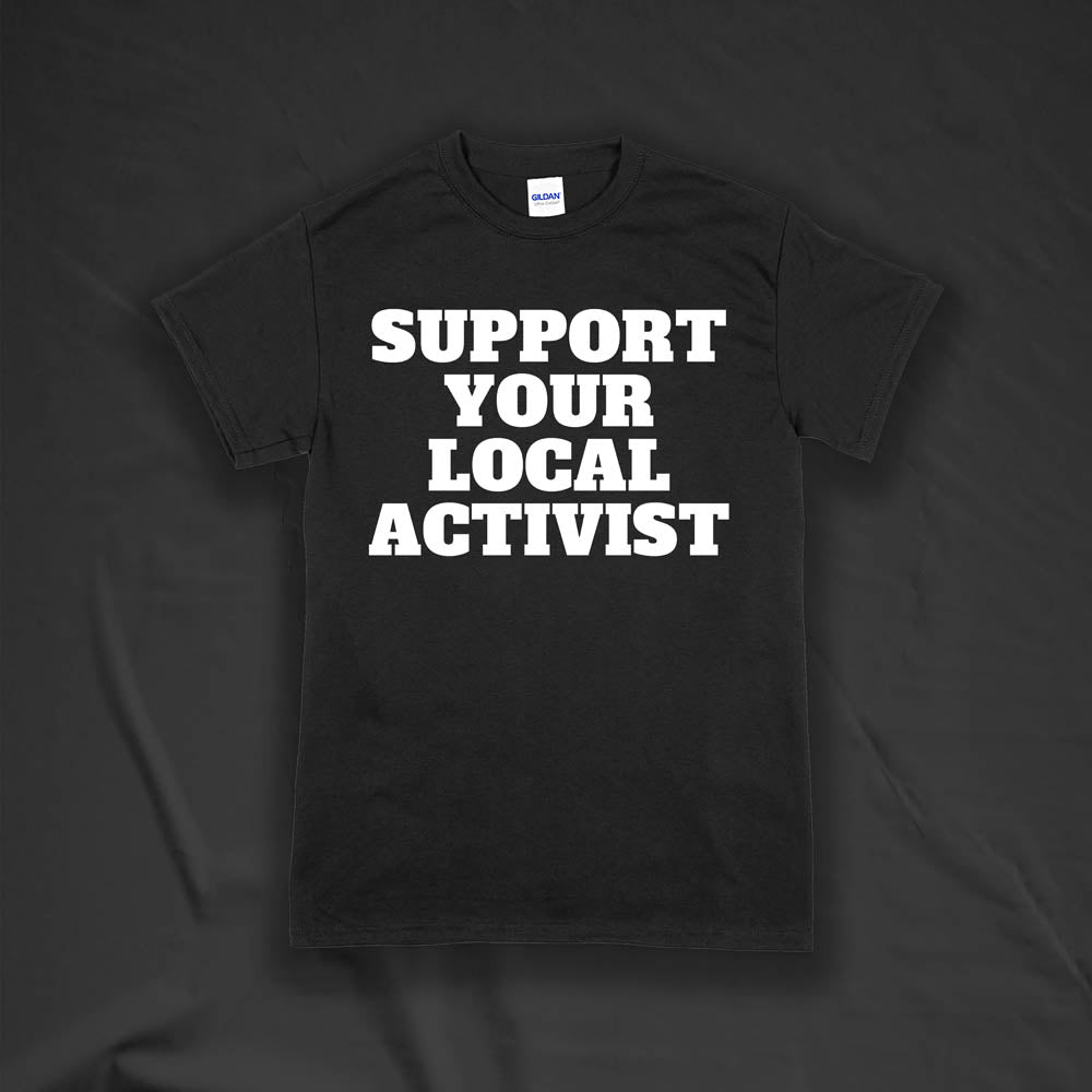 The original Support Your Local Activist t-shirt by LOST. Bold white letters screen printed on a black shirt. The shirt is displayed against a textured black background.