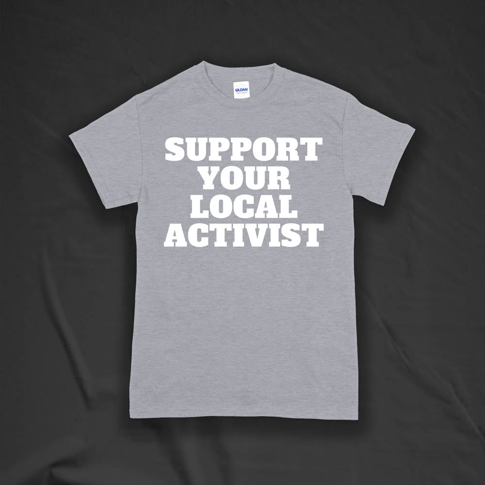 The original Support Your Local Activist t-shirt by LOST. Bold white letters screen printed on a gray shirt. The shirt is displayed against a textured black background.