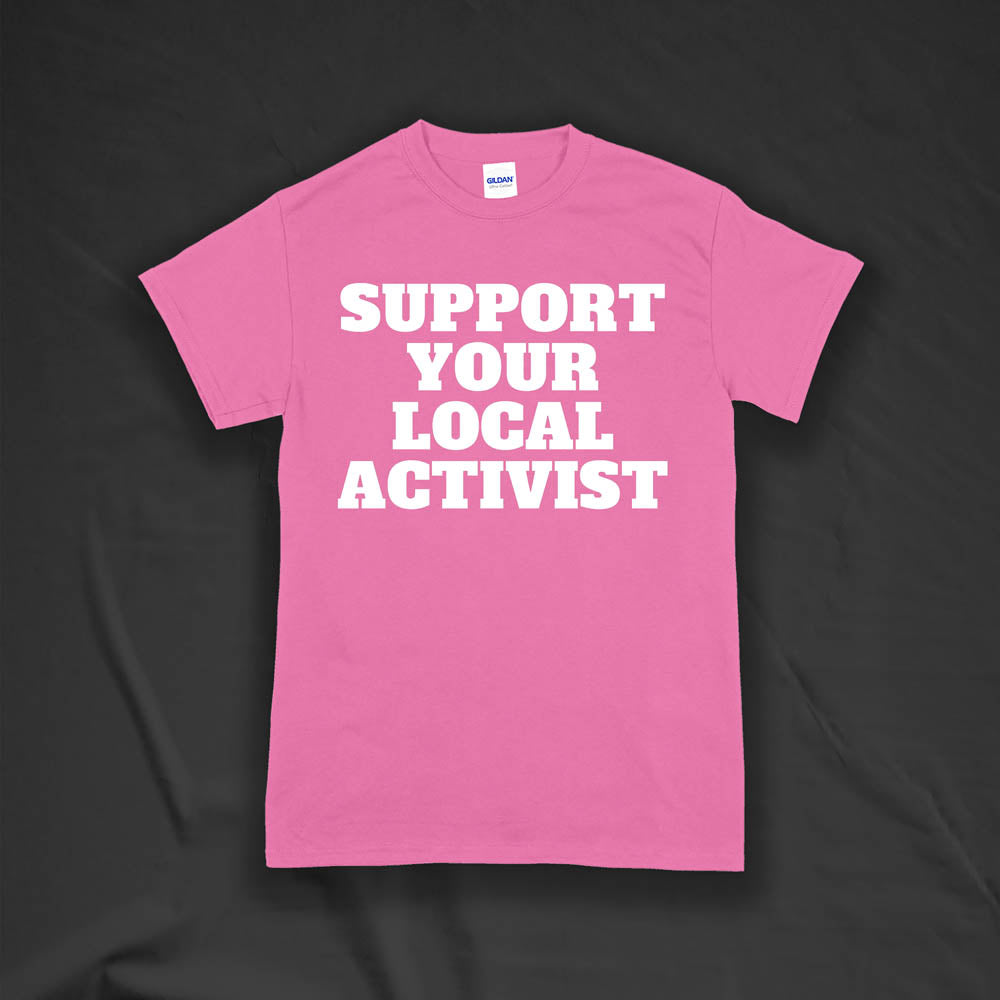 The original Support Your Local Activist t-shirt by LOST. Bold white letters screen printed on a pink shirt. The shirt is displayed against a textured black background.