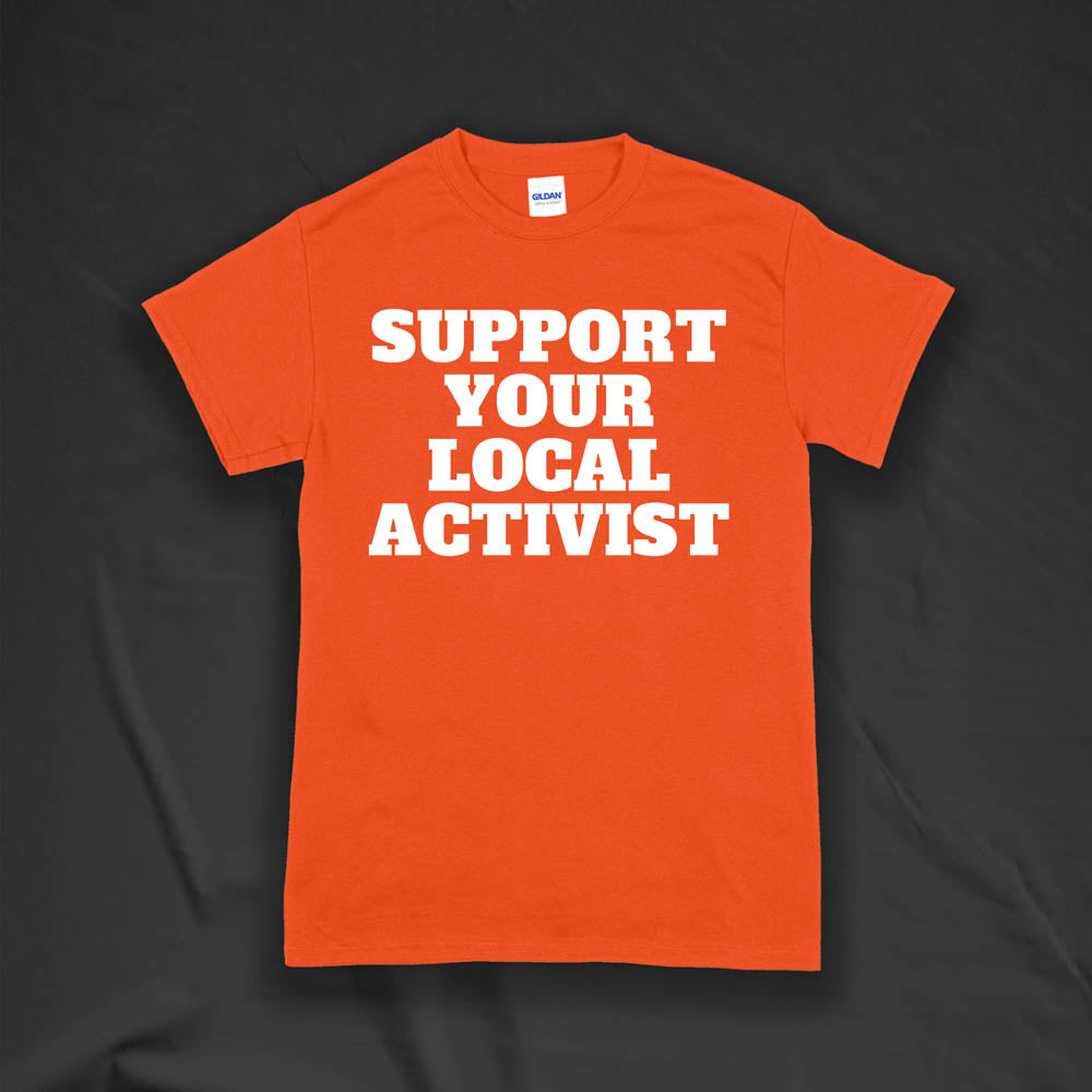 The original Support Your Local Activist t-shirt by LOST. Bold white letters screen printed on an orange shirt. The shirt is displayed against a textured black background.