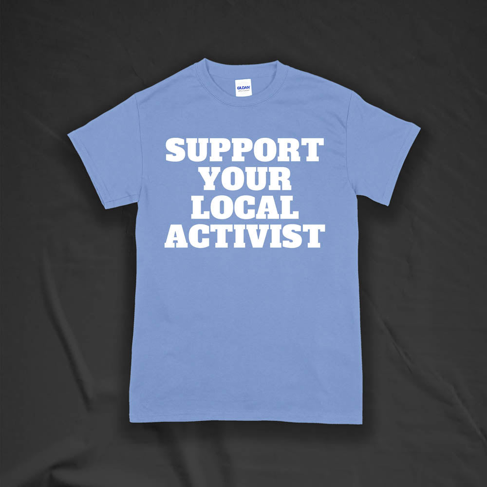 The original Support Your Local Activist t-shirt by LOST. Bold white letters screen printed on a light blue shirt. The shirt is displayed against a textured black background.