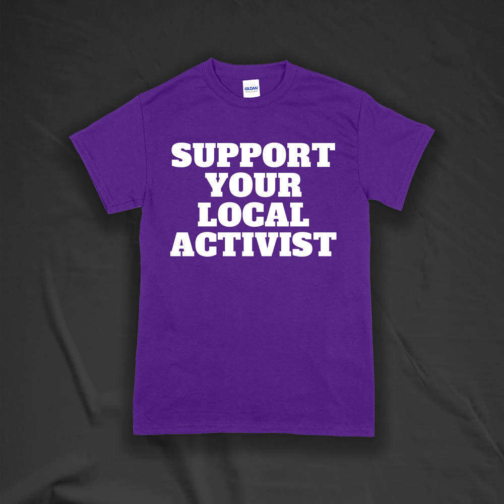 The original Support Your Local Activist t-shirt by LOST. Bold white letters screen printed on a purple shirt. The shirt is displayed against a textured black background.
