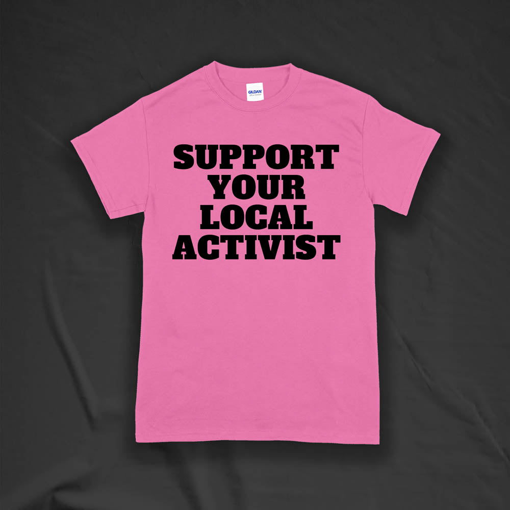 The original Support Your Local Activist t-shirt by LOST. Bold black letters screen printed on a pink shirt. The shirt is displayed against a textured black background.