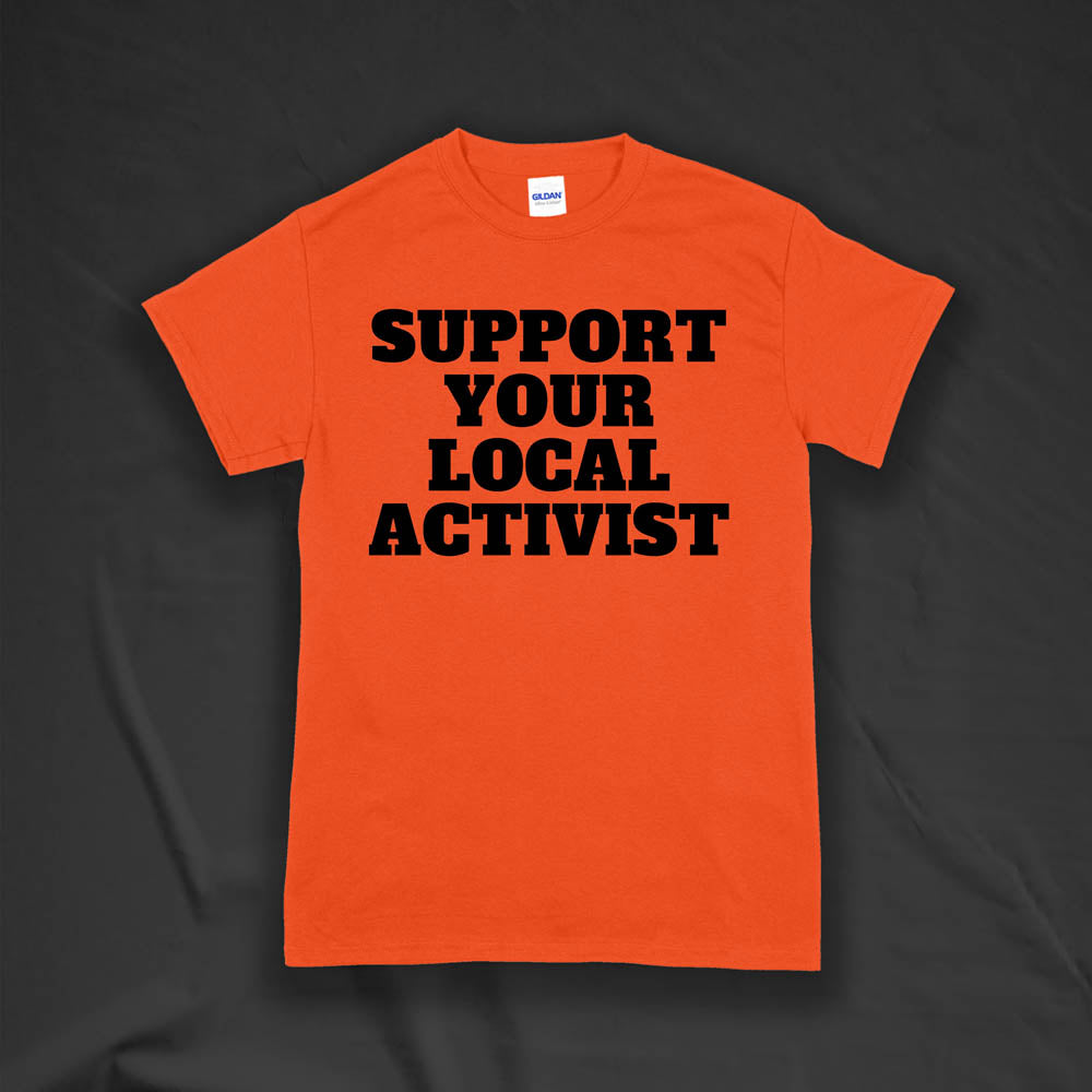 The original Support Your Local Activist t-shirt by LOST. Bold black letters screen printed on an orange shirt. The shirt is displayed against a textured black background.