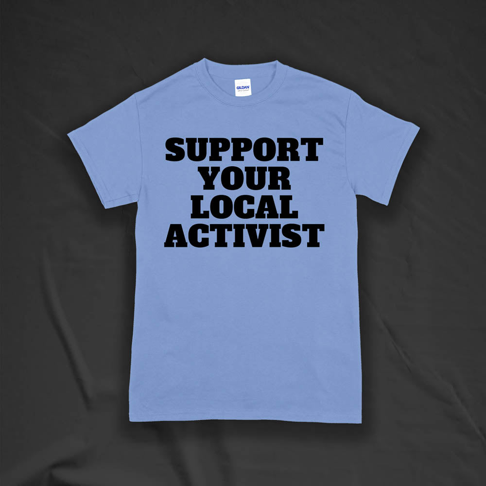 The original Support Your Local Activist t-shirt by LOST. Bold black letters screen printed on a light blue shirt. The shirt is displayed against a textured black background.
