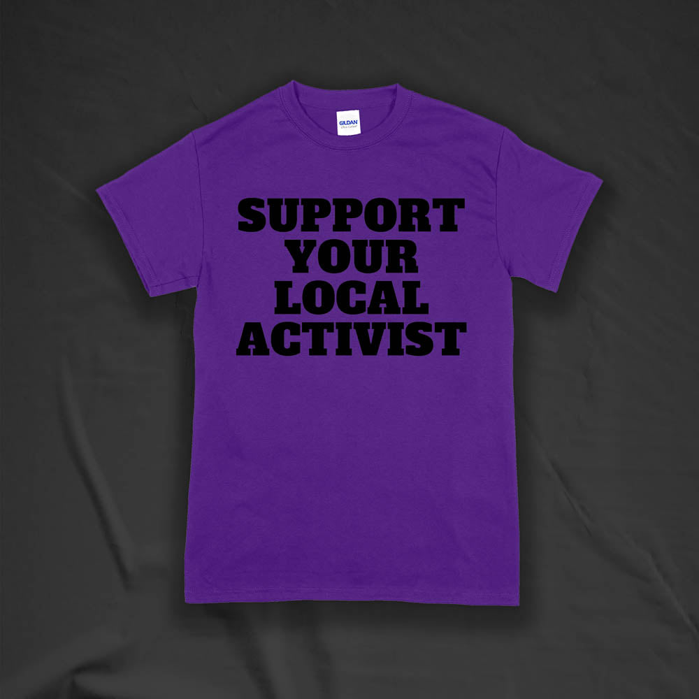 The original Support Your Local Activist t-shirt by LOST. Bold black letters screen printed on a purple shirt. The shirt is displayed against a textured black background.