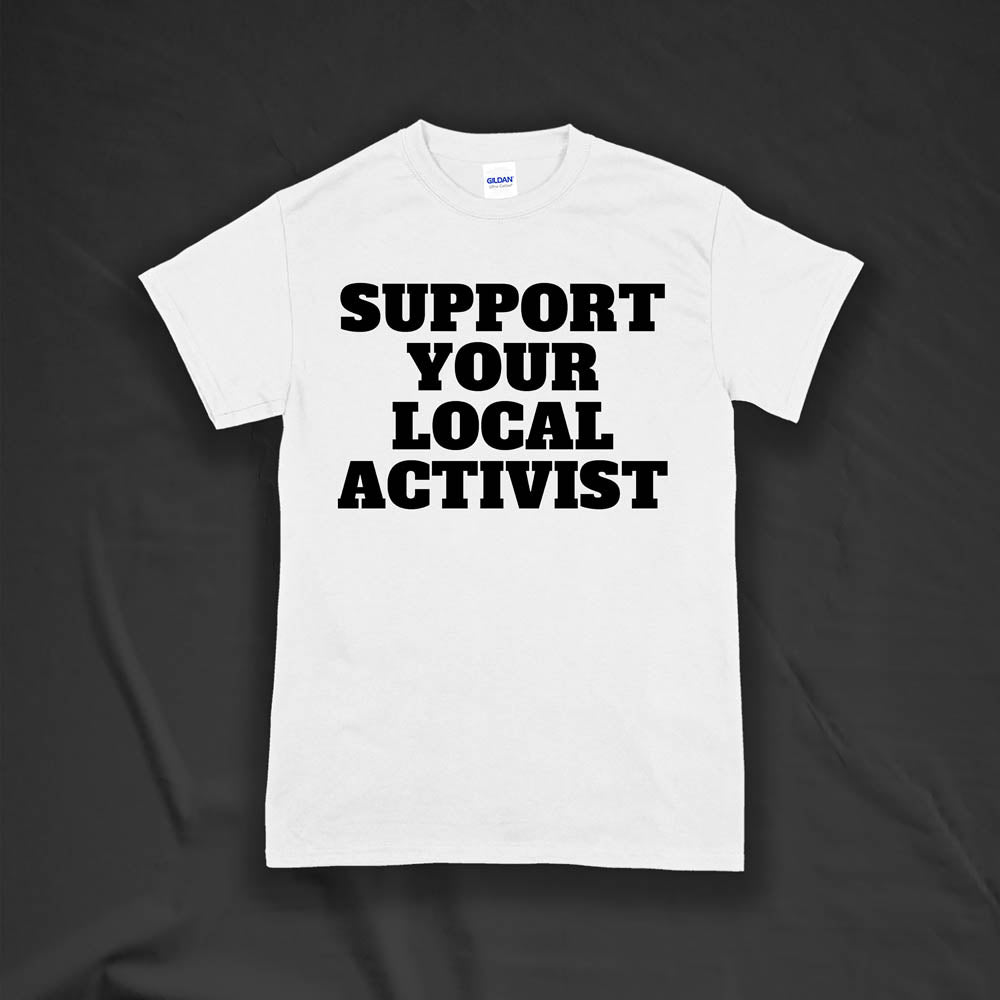 The original Support Your Local Activist t-shirt by LOST. Bold black letters screen printed on a white shirt. The shirt is displayed against a textured black background.