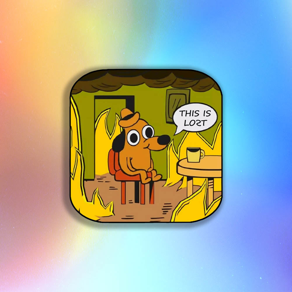 The flaming hot "This Is Fine" internet meme modified to say "THIS IS LOST". The image of a cartoon dog calmly sitting at a table with his coffee while the room burns around him is an accurate portrayal of modern day society. This sticker is set against a holographic background.
