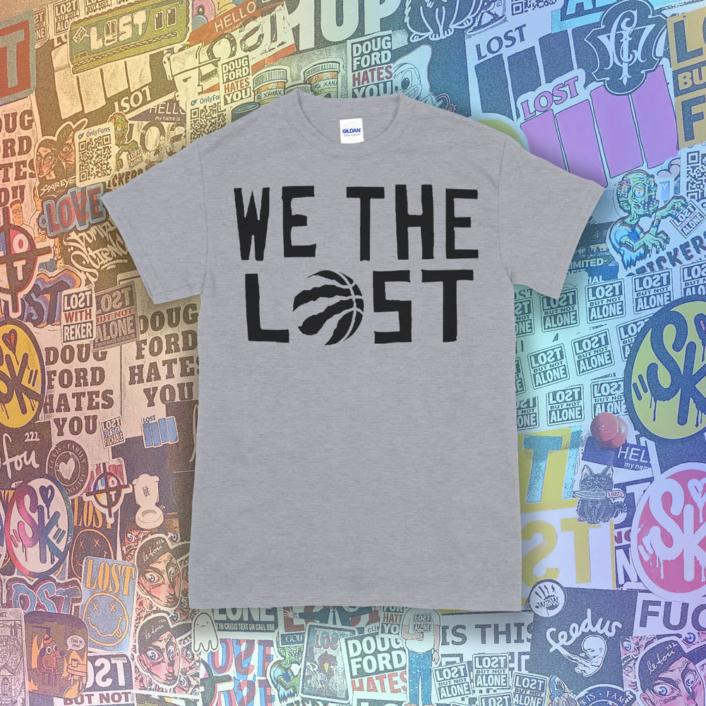 We The Lost t-shirt. Bold black lettering and raptor claw design screen printed on a light gray shirt. A wall of colorful graffiti stickers make up the background.