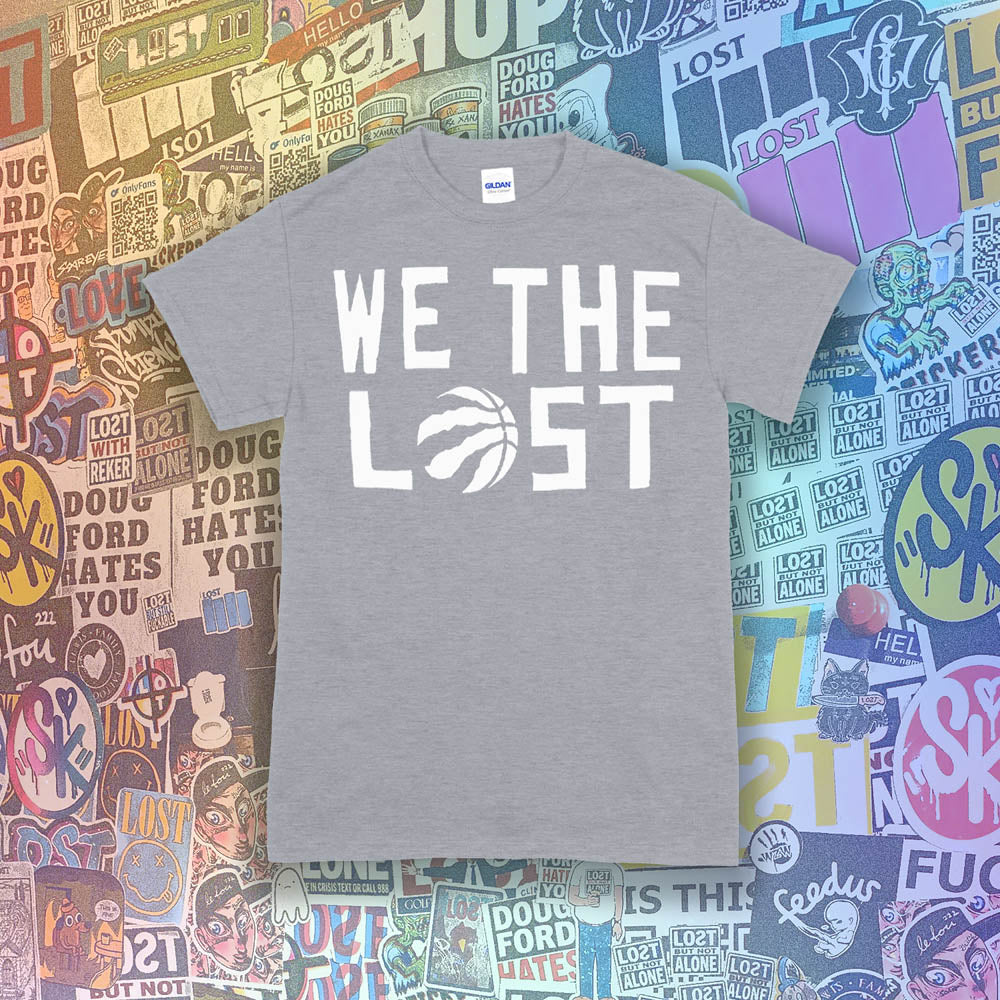 The We The Lost t-shirt. Bold white lettering and raptor claw design screen printed onto a light gray colored shirt. A wall of brightly colored graffiti stickers makes up the background.