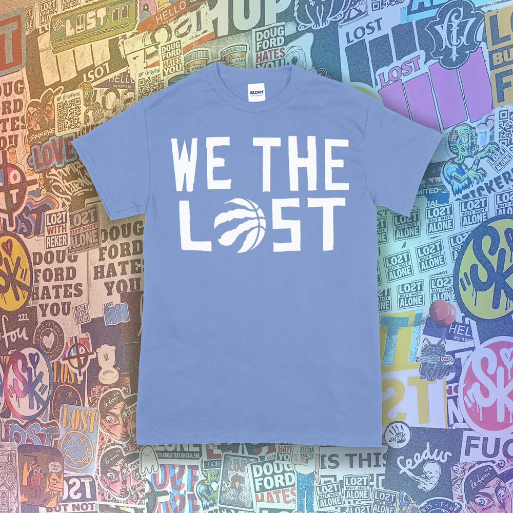 The We The Lost t-shirt. Bold white lettering and raptor claw design screen printed onto a light blue colored shirt. A wall of brightly colored graffiti stickers makes up the background.
